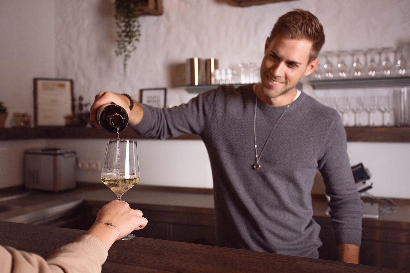 Patrick schenkt einem Gast Wein ein.